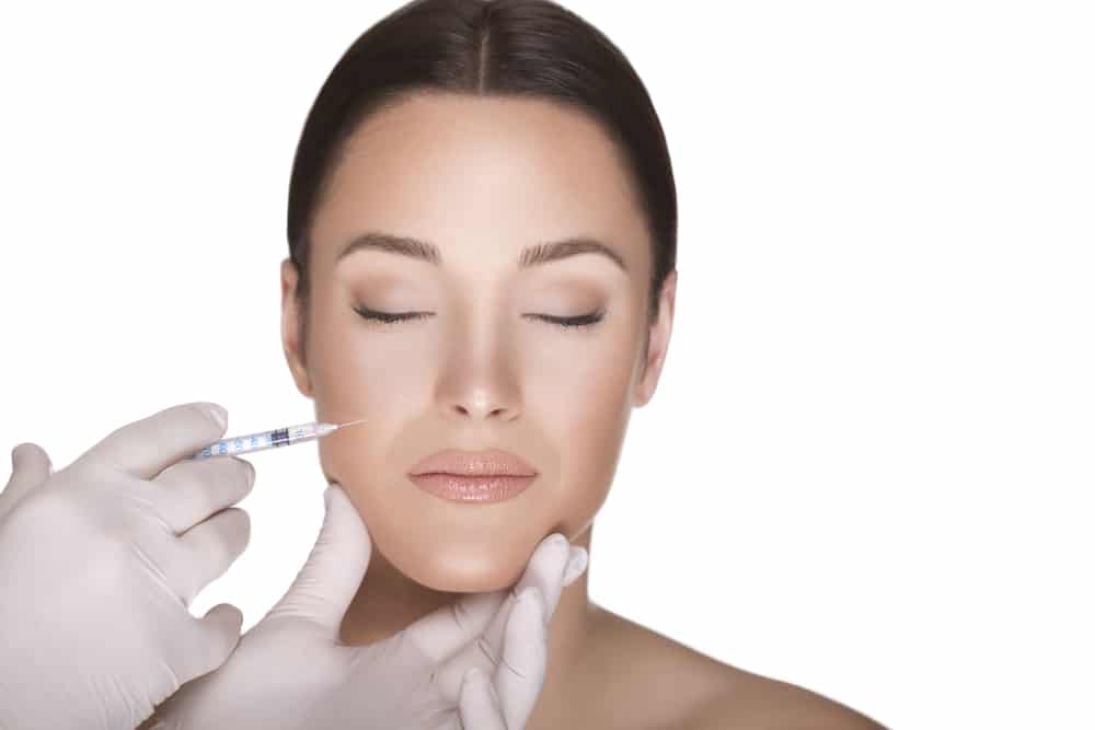 Woman closes her eyes as her injector places Sculptra in her cheeks