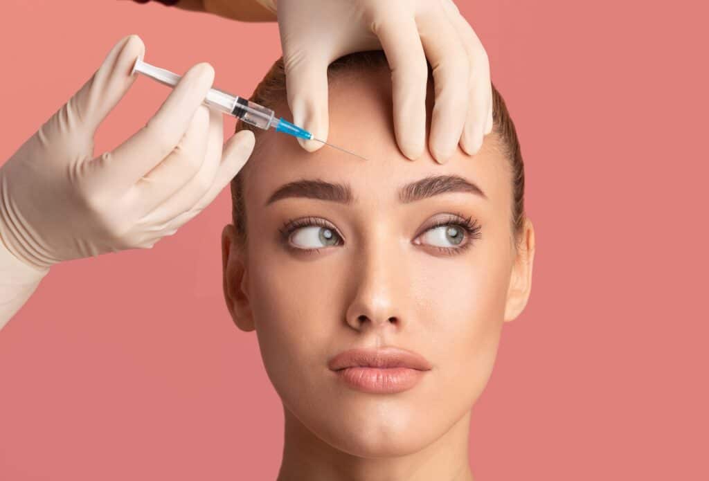 Young woman looks to the side as her Botox injector places a preventive wrinkle treatment in her forehead lines